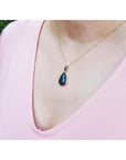 Teardrop-shaped black opal pendant on a gold chain worn by a person in a pink top.
