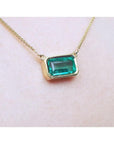 East-west emerald-cut solitaire emerald necklace in 18K yellow gold, bezel set.
