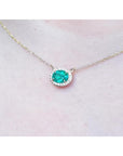 Oval Muzo emerald necklace with diamond halo on a delicate 14K yellow gold chain.