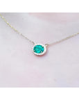 Oval Muzo emerald necklace with diamond halo on a delicate 14K yellow gold chain.