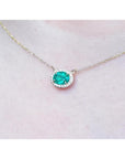 Oval Muzo emerald necklace with diamond halo on a delicate 14K yellow gold chain.