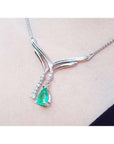14K white gold necklace with a pear-shaped emerald pendant and diamond accents on a chevron design.
