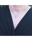 14K yellow gold necklace with a pear-cut emerald and diamond V-chevron pendant on a woman's neck.