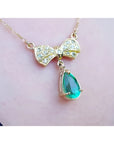 18K yellow gold bow-tie necklace with pave diamonds and a dangling pear-shaped emerald.
