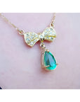18K yellow gold bow-tie necklace with pave diamonds and a dangling pear-shaped emerald.