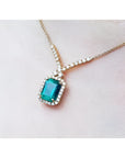 14K yellow gold halo necklace with a rectangular bluish-deep green emerald and natural diamonds.