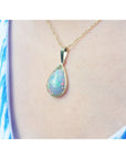 Opal pendant necklace on a person's neck wearing a blue and white patterned top.
