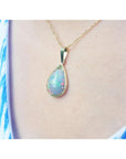 Opal pendant necklace on a person's neck wearing a blue and white patterned top.