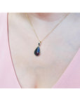 Teardrop-shaped black opal pendant necklace on a person's neck wearing a pink top.