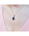 Teardrop-shaped black opal pendant necklace on a person's neck wearing a pink top.