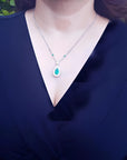 Pear cut emerald necklace with double diamond halo on 18K white gold chain, worn on a woman.
