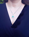 Pear cut emerald necklace with double diamond halo on 18K white gold chain, worn on a woman.