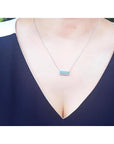 18K white gold necklace with a rectangular emerald-cut Colombian emerald and halo diamonds, worn on a model.
