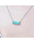18K white gold necklace with a rectangular emerald-cut Colombian emerald and diamond halo, East-West design.