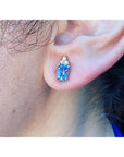 Medium-light blue sapphire and diamond earrings in 14K yellow gold on an ear.