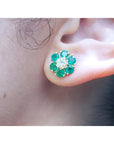 Colombian emerald and diamond cluster earring in 18K yellow gold, worn on an ear.