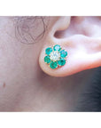 Colombian emerald and diamond cluster earring in 18K yellow gold, worn on an ear.
