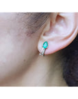 14K white gold clip-on earrings with pear-shaped emeralds and accent diamonds on an ear.
