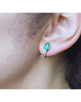 14K white gold clip-on earrings with pear-shaped emeralds and accent diamonds on an ear.