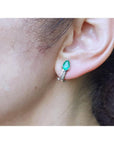 14K white gold clip-on earrings with pear-shaped emeralds and accent diamonds on an ear.