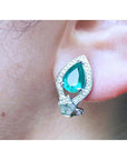 Close-up of a teardrop emerald earring clip-on system on an ear.