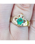 Emerald claddagh ring made of 14k yellow gold on a finger.