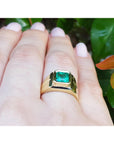 Gold ring with a bezel set emerald on a hand against a natural background