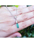 Colombian emerald briolette necklace with a green teardrop pendant held in a hand against a blurred green background