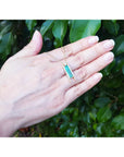 Emerald baguette cut necklace with natural diamonds and 14K yellow gold sliding tube bail shown worn on a person's hand, with a background of green leaves.