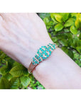 14K yellow gold bangle with round cut Colombian emeralds and diamonds in a floral design.