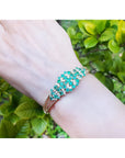 14K yellow gold bangle with round cut Colombian emeralds and diamonds in a floral design.