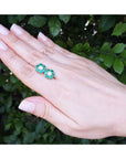 18K yellow gold Colombian emerald and diamond cluster earrings on a hand.