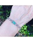 14K white gold paperclip bracelet with a vibrant emerald-cut emerald and diamond halo, worn on a wrist.