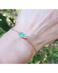 14k yellow gold emerald bracelet with a rectangular green emerald and six small diamonds on a woman's wrist.