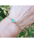 14k yellow gold emerald bracelet with a rectangular green emerald and six small diamonds on a woman's wrist.