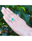 Hand wearing a natural colombian emerald ring in 14k white gold against a leafy background.