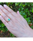 1.27 ct. natural Colombian emerald three-stone ring with trillion diamonds in 18K yellow gold on a hand.