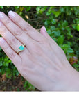 1.27 ct. natural Colombian emerald three-stone ring with trillion diamonds in 18K yellow gold on a hand.