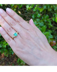 1.27 ct. natural Colombian emerald three-stone ring with trillion diamonds in 18K yellow gold on a hand.