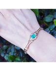 Bracelet with a genuine emerald on a wrist against a leafy background.