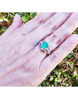 Natural oval emerald ring in 18K white gold with a decorative bridal-style band on a hand.