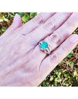 Natural oval emerald ring in 18K white gold with a decorative bridal-style band on a hand.