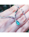 14k white gold necklace with a natural emerald teardrop pendant held in hand against a blurred natural background