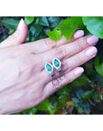 14K gold clip/post earrings with vibrant pear-shaped Colombian emeralds and diamond accents on a hand.