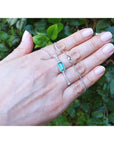 Hand displaying a natural emerald necklace with white gold chain against a green leafy background