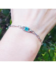 14K white gold paper clip bracelet with a bluish-green emerald and diamond halo on a wrist.