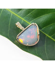 Opal pendant in a gold setting on a green leaf.
