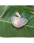 Ethiopian opal gold pendant with prong setting on a green leaf.