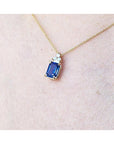 Gold necklace with a rectangular blue sapphire pendant on a person's neck.