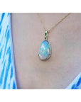 Ethiopian opal pendant with rainbow flashes in 14K yellow gold, worn on a blue and white patterned top.